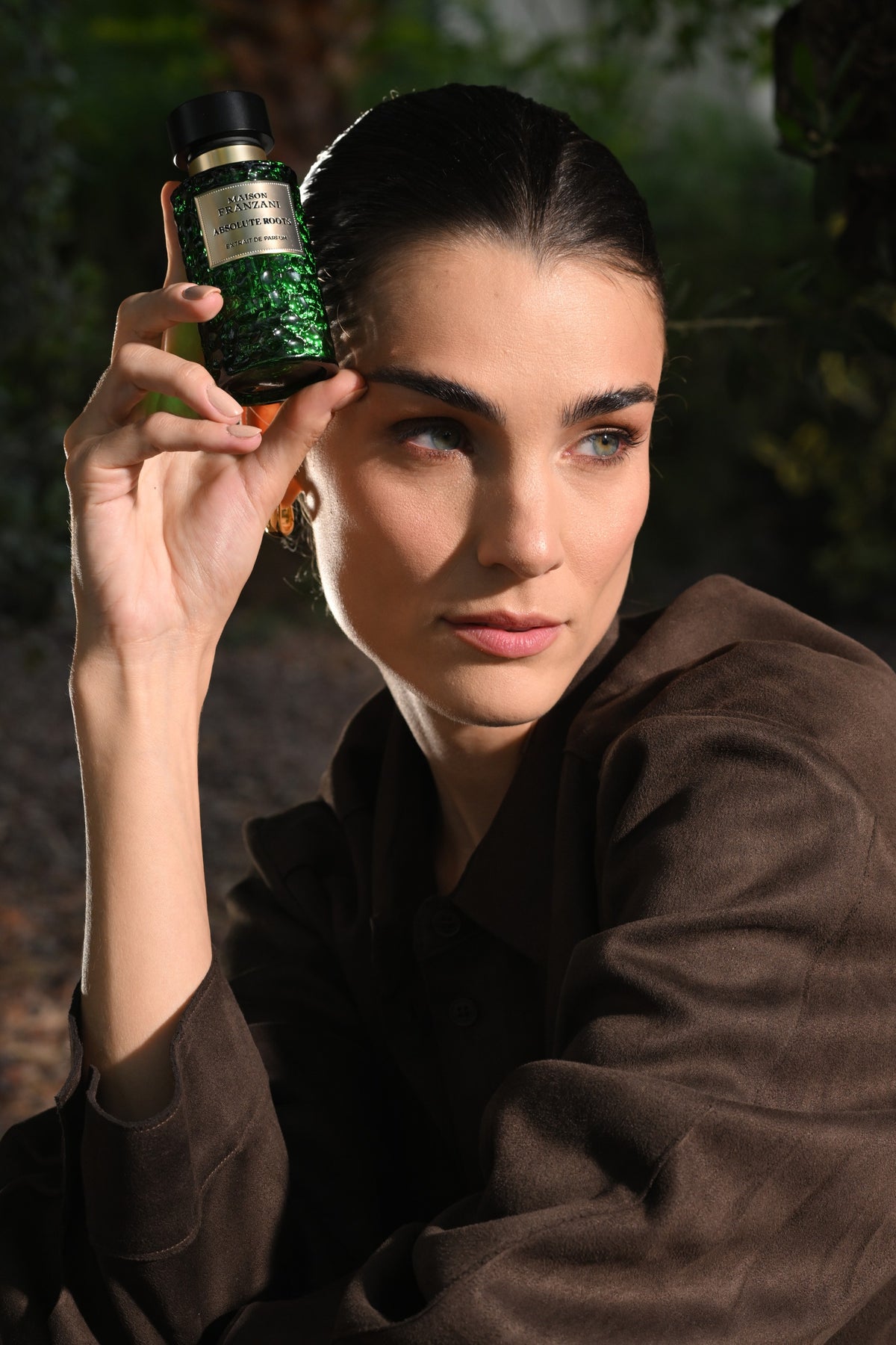 Model mit grünem Absolute-Roots-Flakon neben dem Gesicht.