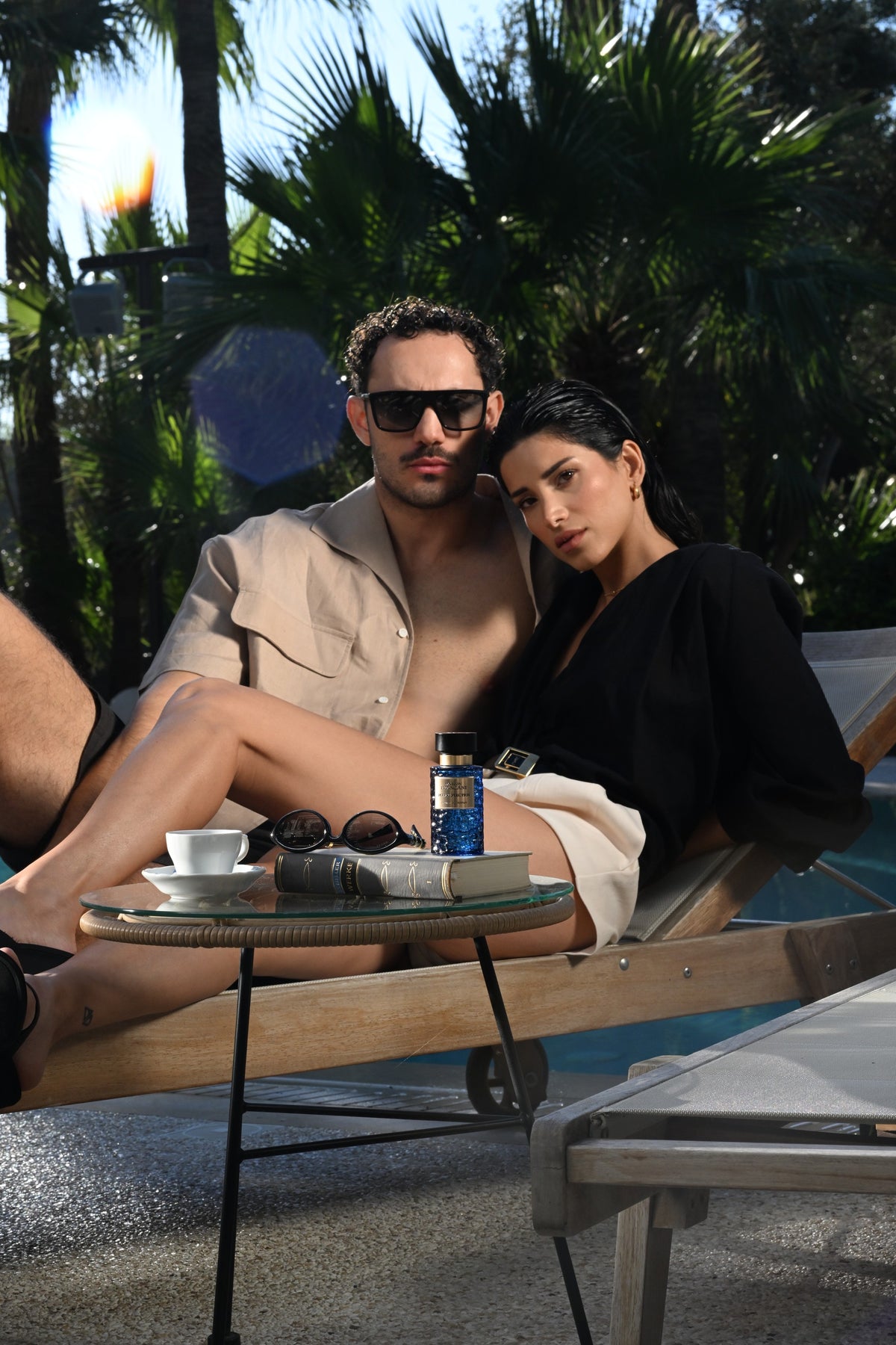Zwei Models auf einer Poolliege mit blauem Parfumflakon auf dem Tisch.
